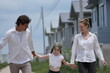 © ultramansk - Cheerful Caucasian family of three lift the girl off the ground swinging her between them on a walk through a new suburban housing development, candid real moment