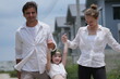 © ultramansk - Cheerful Caucasian family of three swing the child high while walking the sunny street among modern new houses of a suburban housing estate. Concept of family love, care and quality time