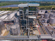 © Amazing Aerial - Aerial view of an industrial facility featuring complex metal structures, storage tanks, and extensive piping systems surrounded by solar panels in Crescentino, Piedmont, Italy.
