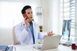 © Fahng - Confident doctor working at the desk on workplace with pc computer at office talking by phone consulting sick patients in medical clinic. Medicine and health concept.
