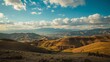 © Art Backgrounds - Panoramic view of rolling golden hills under a bright blue sky with clouds.