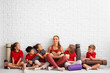 © Pixel-Shot - Female yoga instructor and group of little children sitting near white brick wall