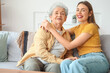© Pixel-Shot - Young woman with her grandmother hugging on sofa at home