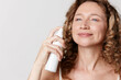 © SHOTPRIME STUDIO - Authentic beauty of a middle aged woman with natural skin, applying a facial spray. Close up on a light background, skincare, wellness, selfcare. soft lighting enhances calm mood.