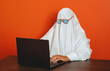 © VISTA by Westend61 - Man in ghost costume types on a laptop at the office