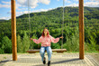 © bondarillia - Person swings on a swing set overlooking a green hill