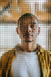 © Westend61 - Portrait of a man looking through textured wire mesh glass