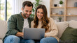 © Vyatcheslav - Happy young couple using a laptop together on a sofa. Smiling man and woman browsing online in a cozy living room