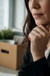 © Eduardo - Close-up vertical portrait of employee on last working day with packed cardboard box on desk, bittersweet expression, natural light, stock photo for career transition and emotional workplace moments