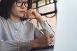 © tippapatt - Close-up of thoughtful businesswoman writing notes using laptop, working remotely in office modern workspace, focused productivity concept.