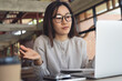 © tippapatt - Confused asian businesswoman gesturing while using laptop in cafe, remote work problem solving concept.