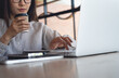 © tippapatt - Asian business woman working on laptop while drinking coffee in cafe, modern workspace, focused remote work, online business concept.