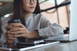 © tippapatt - Asian businesswoman working on laptop while drinking coffee in cafe, modern workspace, focused remote work, online business concept.