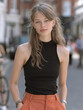 © visoot - Young woman with long wavy hair, wearing sleeveless black top and orange pants, standing outdoors on city street, confident expression