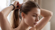© Rhallyson - Close-up shot of a young woman with light brown hair tying it into a ponytail using a black spiral hair tie.