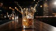 © Imam Muaziz - A glass of whiskey with ice cubes splashing on a wooden bar counter.