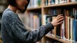 © Thares2020 - A person browsing books on a wooden shelf in a library or bookstore setting with focused attention