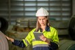 © BESTIMAGE - Worker inspecting metal sheet machine performance checklist operation system inspection in factory Female engineer wearing hardhat and safety jacket checking inventory on tablet at storage site