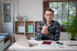 © Tj - Mature man working at a home office desk, focusing on a laptop and documents, representing remote work, online learning, or financial management