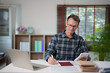 © Tj - Senior man analyzing financial data and managing personal finances at home, using a laptop, calculator, and notebook for planning expenses and savings