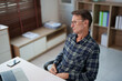 © Tj - Senior man in eyeglasses and plaid shirt sitting at a desk, contemplating a thought or looking away from his laptop, considering new ideas for his work, business, or personal life goals