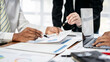 © Freedomz - Three people are sitting at a table with papers and laptops