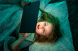 © Volodymyr - Child using tablet in bed. Kid holding tablet while lying at night. Teenager watching tablet screen in bed. Child playing games on tablet at night.
