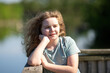 © Volodymyr - Child portrait shows peaceful summer mood. Smiling child enjoys warm sunlight outdoors. Relaxed child looks toward green nature. Child expression feels joyful and calm.