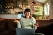 © Davor - Smiling woman on laptop video call in cozy home living room