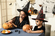 © Pixel-Shot - Little girl with her mother painting Halloween pumpkins in kitchen