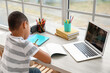 © Pixel-Shot - Little African-American boy studying online with laptop at home