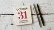 © irha - Halloween October 31 calendar page on white wood. Vintage tear-off calendar date with pens. Autumn holiday planning and scheduling concept.
