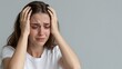 © mihrzn - A woman experiencing emotional pain, tears streaming down her face as she grips her head with both hands against a plain background.