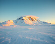 © MediaPro - Sommet montagneux isolé recouvert de neige immaculée se dressant au-dessus d'une vaste plaine glacée, ciel rose pastel au crépuscule créant une atmosphère paisible et minimaliste