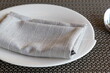 © photoranger2521 - Close-up of modern table setting with grey fabric napkin on a white plate and placemat background.