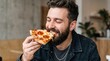 © Taras Roshchuk - A man smiles while taking a bite of a pepperoni pizza slice in a relaxed indoor space. He is dressed casually and appears pleased. The background shows a simple decor