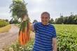 © TrueShot | Westend61 - Smiling grandfather holds fresh carrots in the sunny vegetable garden