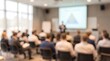 © CuteBee - Business people sitting in conference room listening to presentation with blurred foreground and screen focus representing professional corporate training and educational seminar event