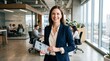 © Ziqri - Smiling professional businesswoman holding a digital tablet with charts in a modern corporate office.