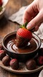 © Guzel - A hand dipping a ripe strawberry into a ceramic bowl of melted chocolate surrounded by dusted raspberries on a rustic wooden table, sweet culinary indulgence, romantic dessert, Valentine's Day.