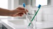 © Most. Hamida Khatun - A person reaching for a toothbrush in a glass on a clean white bathroom vanity counter top