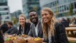 © Alexei - Group of three professionals enjoying lunch outdoors at a modern urban setting, with healthy food in eco-friendly containers on wooden picnic tables