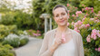 © Len_mik - Smiling woman with short hair holding a pink ribbon in a garden. Breast cancer survivor outdoors. Health awareness and oncology recovery concept