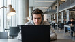 © Celt Studio - focused young male college student wearing wireless headphones typing laptop computer sitting busy university library studying hard preparing difficult exam