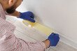 © Pixel-Shot - Young male decorator applying masking tape to baseboard at home, closeup