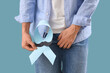 © Pixel-Shot - Young man with blue ribbon and paper mustache on color background, closeup. Prostate cancer awareness concept