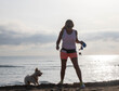 © Luis - Woman walking with a small white dog by the ocean during an active morning sunrise