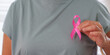 © Natee Meepian - Cropped hand holding pink ribbon on chest for breast cancer awareness