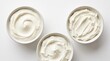 © Wati - Three Bowls of Creamy White Yogurt or Sour Cream with Swirls on a White Background