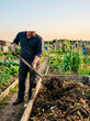 © DriftPixels - A man is turning compost in a wooden bin within a community garden in a lush outdoor garden setting